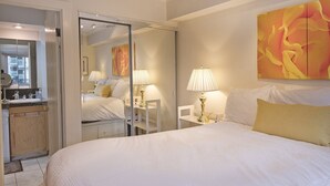 Une chambre d’hôtel avec un grand lit, une table de chevet avec une lampe, un miroir et une salle de bain avec un lavabo et un miroir.