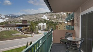 Un balcon donnant sur un paysage montagneux, une table avec des chaises et un bâtiment doté d’une balustrade verte.