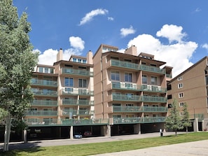 A multi-story residential building with balconies, a covered parking area, and a clear sky. - Vantage Point Condo 307 (Vail)