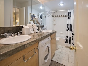 A modern bathroom with two sinks, a mirror, a washing machine, and a shower area. - Vantage Point Condo 307 (Vail)