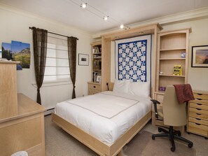 A bedroom with a bed, a desk, a chair, a bookshelf, and a quilt on the wall. - Vantage Point Condo 307 (Vail)