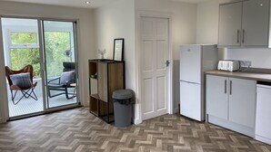 Uma cozinha moderna com piso em padrão herringbone, uma geladeira, uma torradeira e uma porta de vidro deslizante que dá para uma área externa com uma cadeira.