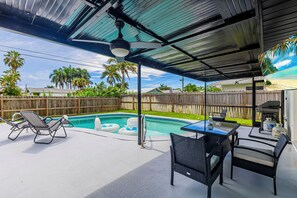 Une terrasse couverte avec une piscine, des chaises longues et une table.