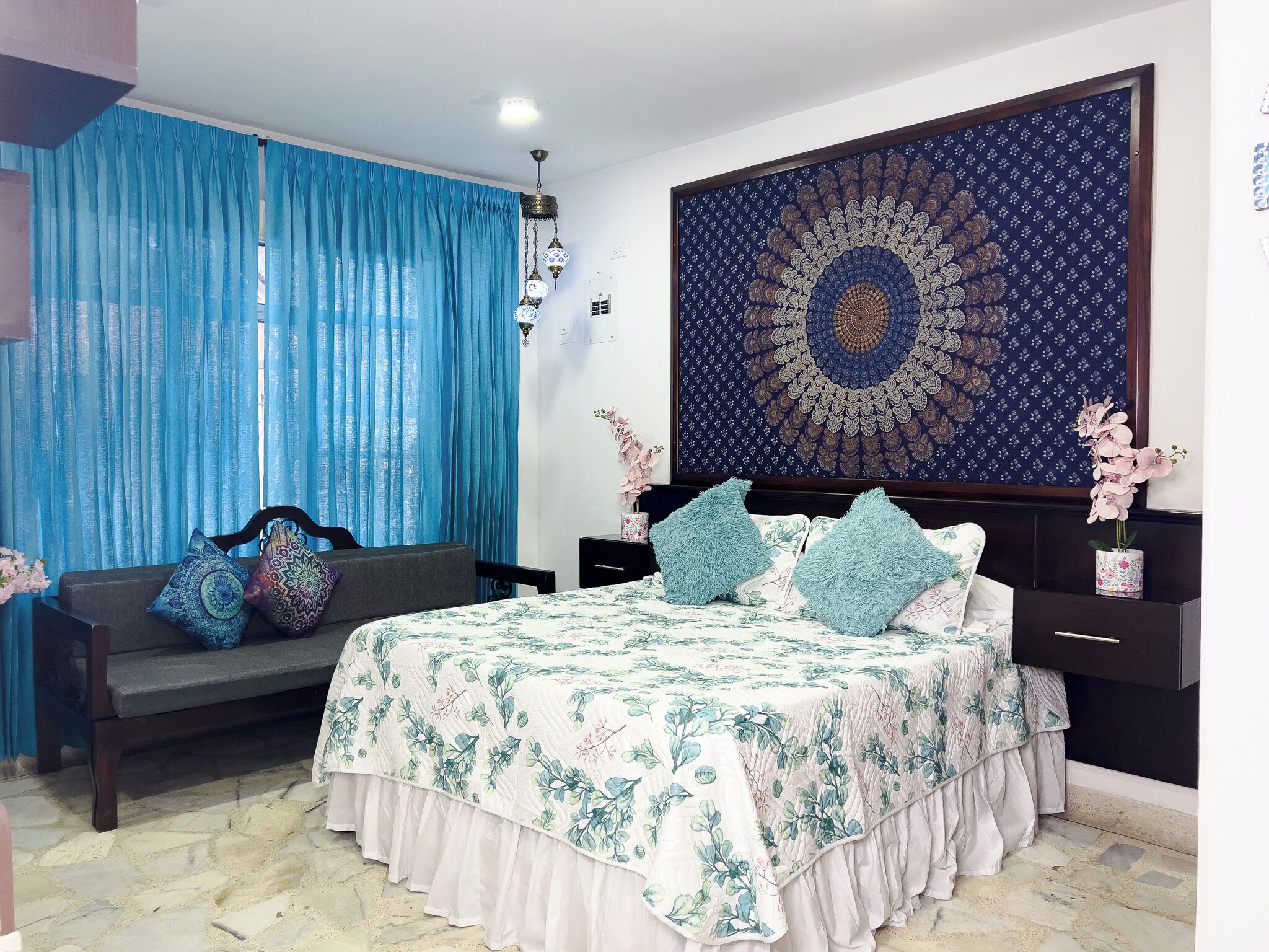 A bedroom with a bed, a sofa, a large tapestry, and a nightstand.
