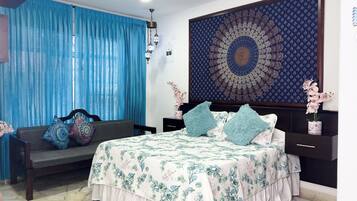 A bedroom with a bed, a sofa, a large tapestry, and a nightstand.