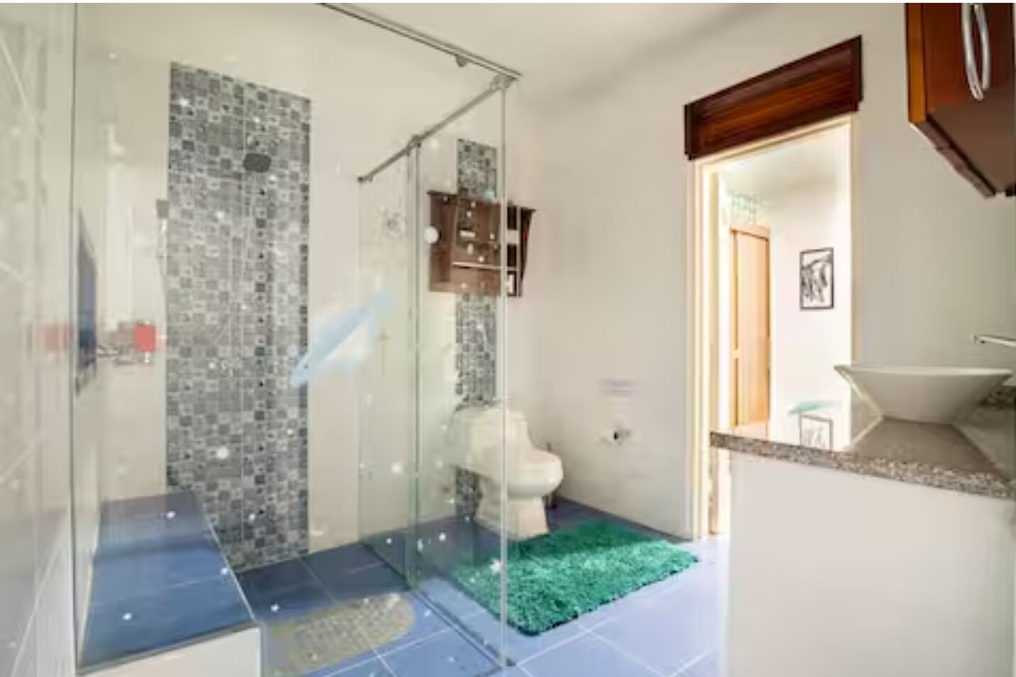 Une salle de bain moderne avec une douche à parois de verre, des toilettes blanches et un tapis vert.