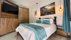 A bedroom with a bed, wooden wardrobe, cityscape painting, and a hanging light fixture.
