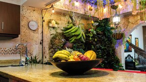Een keuken met een fruitschaal op het aanrecht, een klok aan de muur en hangende planten.