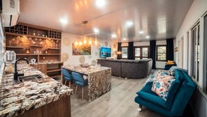 A modern kitchen with a marble countertop, a dining area with blue chairs, a grey sofa, and a large window. - Modern Luxurious Apt With Spa Near Chipichape (Cali)