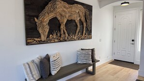 A hallway with a wooden bench, a large wooden sculpture of a horse, and a white door.
