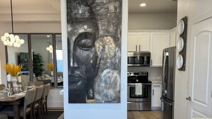A modern kitchen with stainless steel appliances, a dining area with a white table and chairs, and a large abstract painting on the wall.