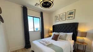 A neatly arranged hotel room with a large bed, a bedside table with a lamp, and a window with curtains.