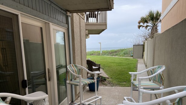 A patio area with white chairs and a table, a patterned rug, and a view of the ocean. - Wave Action!Condo on the Beach w/Umbrella Service next to famous Wanna Wanna Bar (South Padre Island)