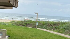 A grassy area with a path leading to the beach, a bench, and a signpost. - Wave Action!Condo on the Beach w/Umbrella Service next to famous Wanna Wanna Bar (South Padre Island)