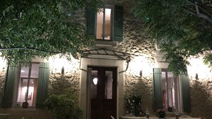 A stone building with a wooden door and green shutters, surrounded by potted plants and outdoor seating. - Farm house, 5 miles from Avignon! Vineyard (Jonquerettes)