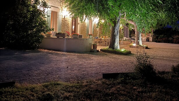 A stone building with a large tree in front, a paved driveway, and outdoor seating area with tables and chairs. - Farm house, 5 miles from Avignon! Vineyard (Jonquerettes)