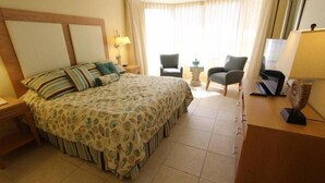 A hotel room with a large bed, a desk, two chairs, a TV, and a lamp.