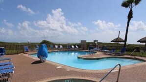A swimming pool with lounge chairs and umbrellas, surrounded by a brick deck.