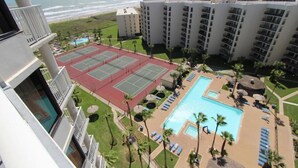 A hotel with a tennis court, pool, and ocean view.