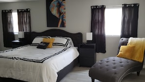 Ein Schlafzimmer mit Bett, Nachttischen, einem Sessel und einem Fenster mit Vorhängen.