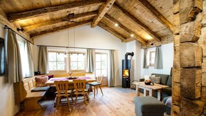 Uma cabana acolhedora, com interior em madeira, área de jantar com mesa e cadeiras, lareira e parede de pedra.