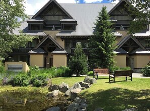 A lodge with a symmetrical facade, multiple balconies, and a well-maintained garden with a pond and benches. - Lagoons Family Retreat (Whistler)