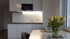 Una cocina moderna con armarios blancos, microondas y un lavabo. Hay una mesa de comedor con un jarrón de tulipanes y una tetera.