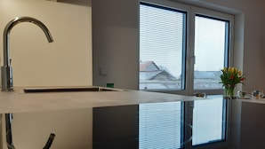 Una cocina moderna con encimera reflectante, grifo de acero inoxidable y ventana con persianas.