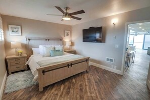 Une chambre à coucher avec un lit en bois, des tables de chevet, un ventilateur de plafond, un téléviseur à écran plat et une vue sur une autre pièce.