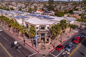 A multi-story building with a flat roof, surrounded by palm trees and a street with cars and a traffic light.