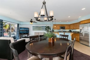 A modern kitchen with wooden cabinets, a stainless steel refrigerator, and a dining area with a round table and chairs.