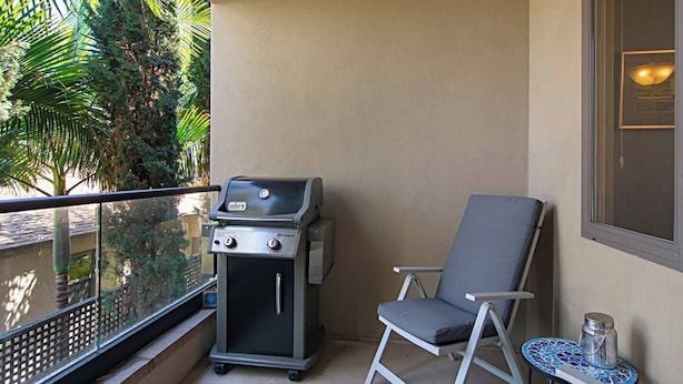 Een balkon met een barbecue, een stoel en een tafeltje met een decoratief object.