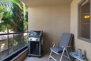 Un balcone con una griglia, una sedia e un piccolo tavolo con un oggetto decorativo.