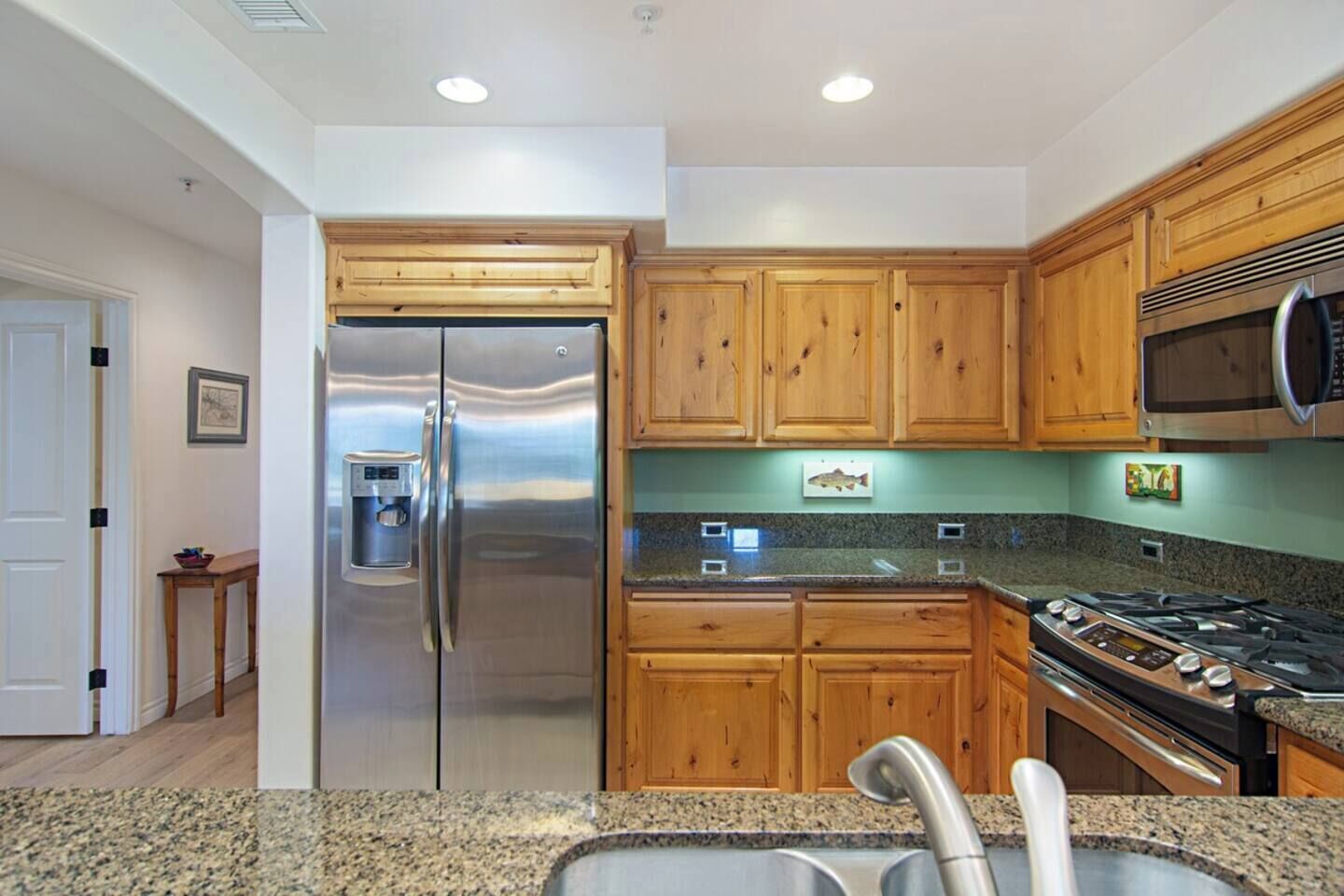 A kitchen with wooden cabinets, stainless steel appliances, granite countertops, and a stainless steel sink.