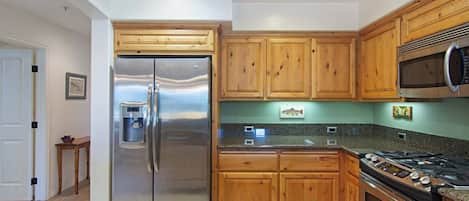 A kitchen with wooden cabinets, stainless steel appliances, granite countertops, and a stainless steel sink.