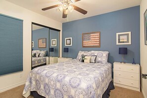 Un dormitorio con una cama grande, un ventilador de techo, un espejo y una pared decorada con cuadros.