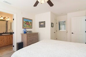 Een slaapkamer met een groot bed, een kaptafel, een spiegel en een plafondventilator.