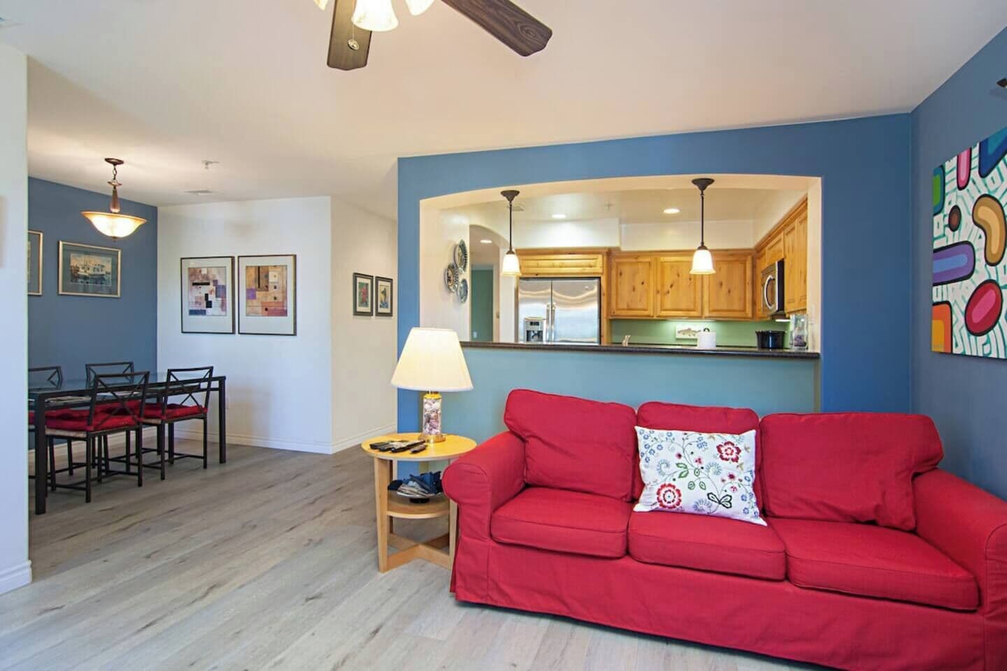 A living room with a red sofa, a dining area with a table and chairs, and a kitchen with wooden cabinets.
