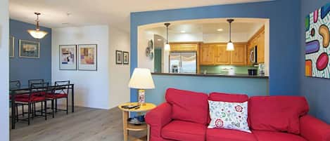 A living room with a red sofa, a dining area with a table and chairs, and a kitchen with wooden cabinets.