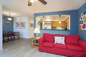 Een woonkamer met een rode bank, een eethoek met een tafel en stoelen, en een keuken met houten kastjes.