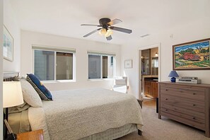 Een slaapkamer met een bed, een kaptafel, een bureau, een stoel, een plafondventilator en een schilderij aan de muur.