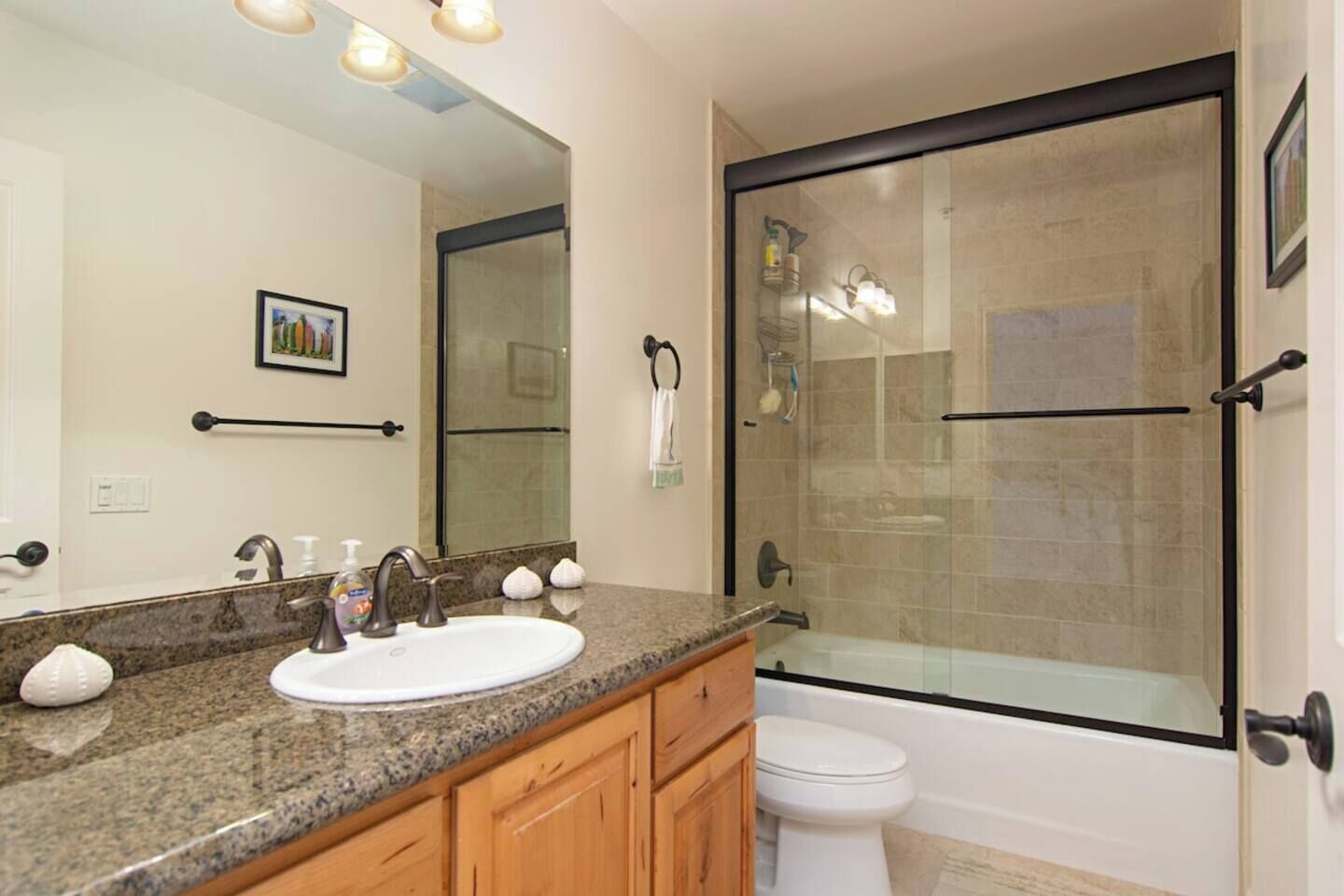 A bathroom with a granite countertop, a white sink, a glass-enclosed shower, and a toilet.