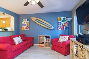 Een woonkamer met rode banken, een boekenkast, een surfplank en abstracte wanddecoratie.
