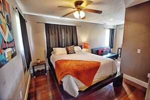 Hotelkamer met een bed, een plafondventilator, een nachtkastje, een lamp en een raam met gordijnen.