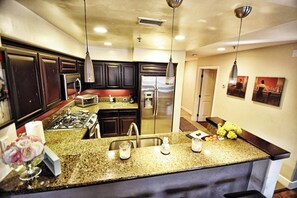 Une cuisine dotée de plans de travail en granit, d’appareils électroménagers en acier inoxydable, d’armoires en bois foncé et de luminaires suspendus.