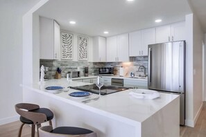 A modern kitchen with white cabinetry, a stainless steel refrigerator, and a central island with bar stools.