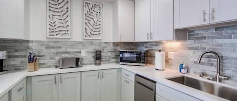 A modern kitchen with white cabinets, a stainless steel sink, and a brick backsplash.