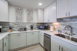 A modern kitchen with white cabinets, a stainless steel sink, and a brick backsplash.