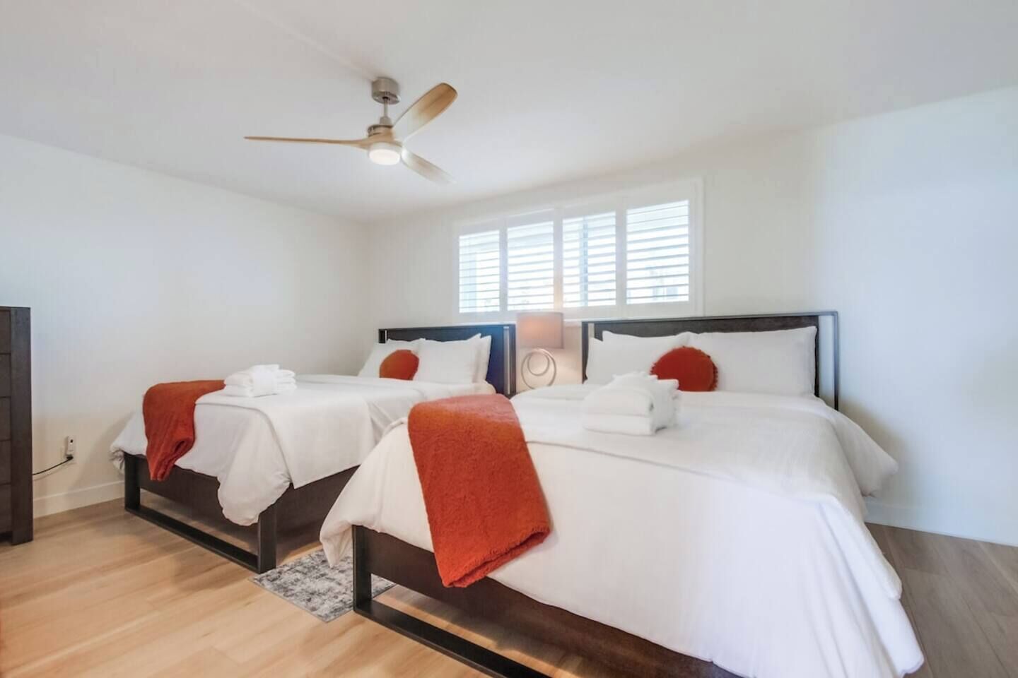 A hotel room with two beds, a ceiling fan, and a window with blinds.