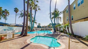 A swimming pool area with palm trees, a brick walkway, and a building with a white fence. - New photos! Oceanfront condo with parking and pool (San Diego)
